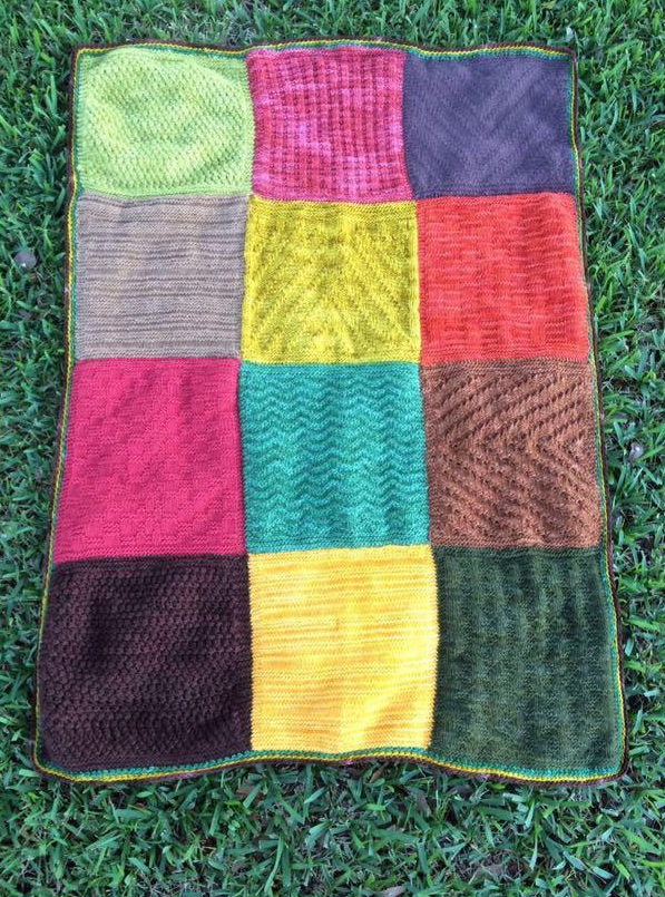 A patchwork knitted blanket arranged on grass